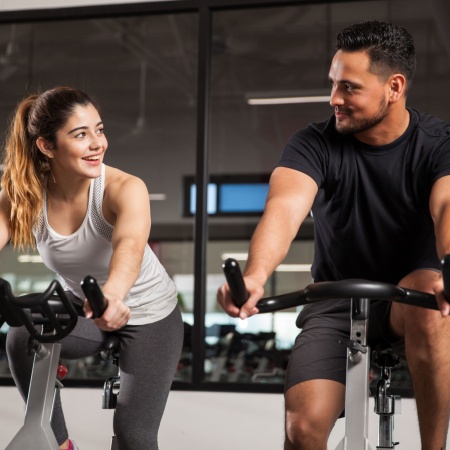 A man and woman give each other a lingering look while sitting on bikes in spin class