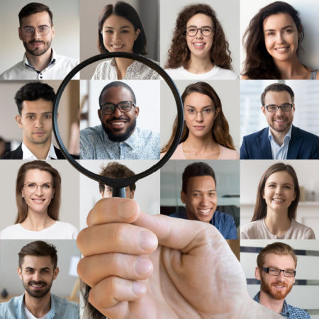 Hand with magnifying glass over picture of 16 men and women