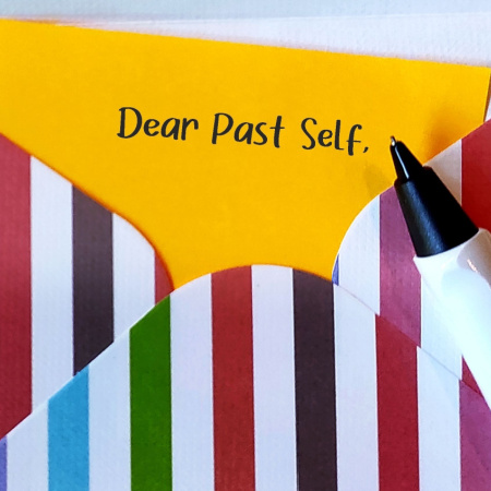 Yellow notecard with "Dear Past Self" written on it. Notecard is in striped, rainbow-colored envelope.