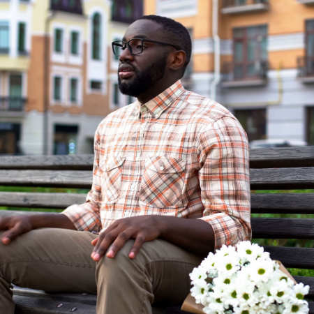 Man sitting on park bench with flowers next to him, looking scared about upcoming first date