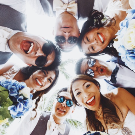 Group of friends in circle, at a wedding, smiling looking down at camera
